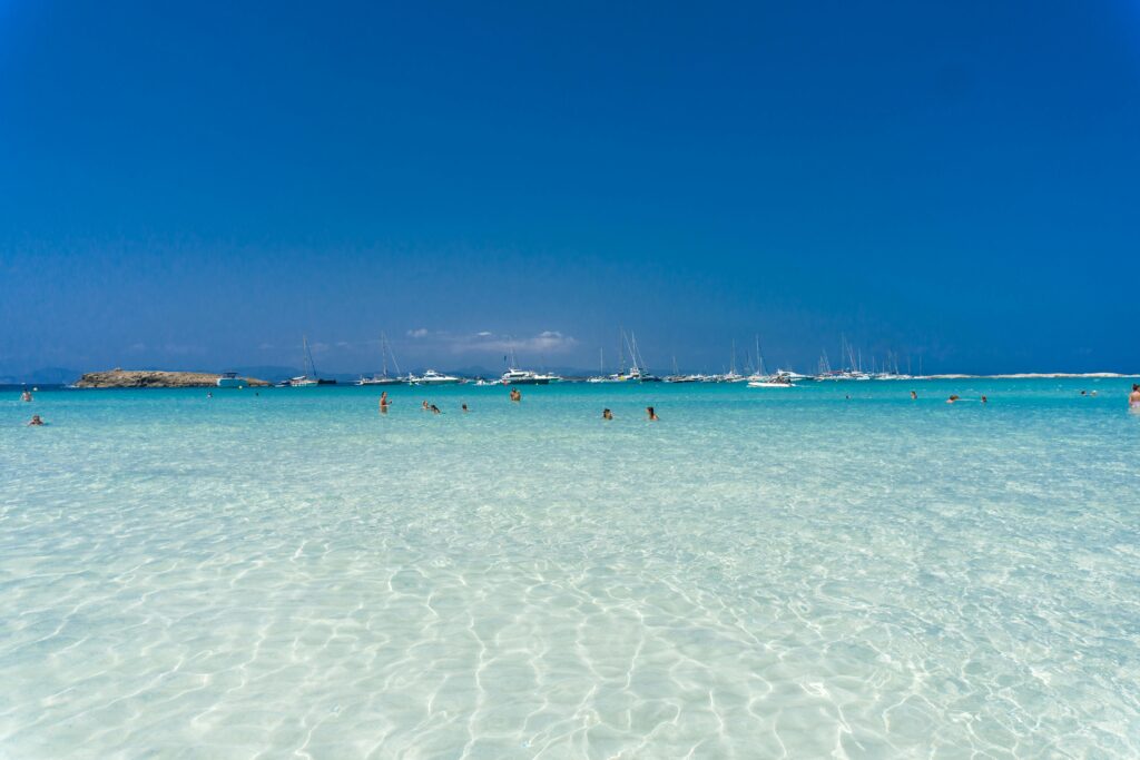 Enjoy leisure time at a Spanish beach with turquoise waters and distant yachts, perfect for summer vacation.